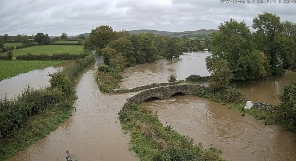 Flood: Generative AI raises alert. Next timed capture. Generative AI reports the river over its banks and water across the whole carriageway, level about 1.8 m. The level rule fires: road-closure alert to the operations team and the highways authority.